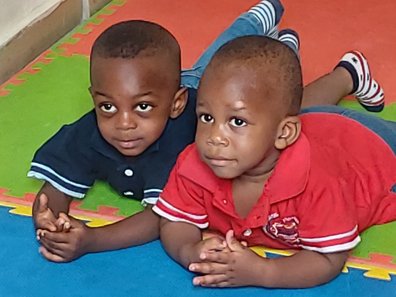 Two small friends lying side by side on the bright play mat