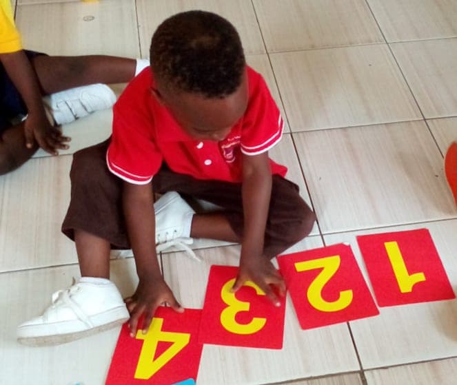 A pupil arranging large number cards on the floor during a counting activity